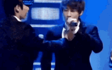 a man in a suit is holding a microphone in front of another man in a suit