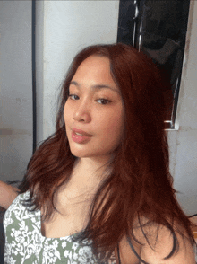 a woman with long red hair is wearing a floral top