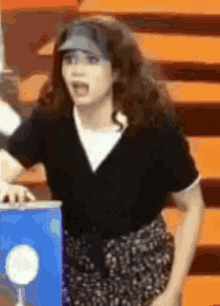 a woman wearing a visor and a black shirt stands in front of a blue box