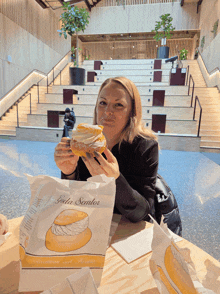 a woman sitting at a table holding a donut and a bag that says ' gala semlor ' on it