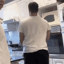 a man in a white shirt stands in front of a microwave in a kitchen