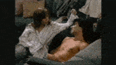 a man without a shirt is laying on a couch with a woman standing behind him .