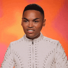 a man wearing a white jacket with studs on it looks at the camera