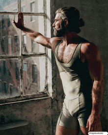 a man in a tank top and shorts leans against a window looking out