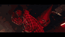 a man in a plaid shirt is standing in a dark room with his arms outstretched .