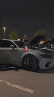 a white car with its hood open is parked in a parking lot at night .