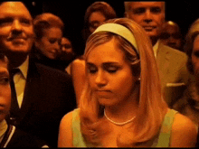 a woman wearing a headband and a pearl necklace is sitting in a crowd of people .