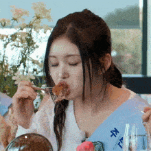 a woman wearing a blue sash with chinese writing on it is eating food with a fork