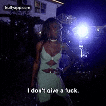 a woman in a green dress is standing in front of a building at night and saying `` i don 't give a fuck ''