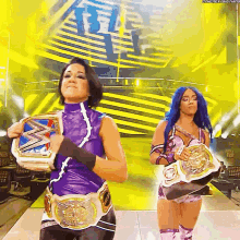two female wrestlers are holding their championship belts in front of a yellow background .