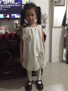 a little girl in a white dress stands in front of a tv screen that says " toto "
