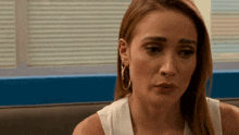 a woman in a white tank top and hoop earrings is sitting at a table .