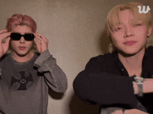 a man wearing sunglasses stands next to another man wearing a sweatshirt with a cross on it