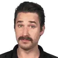 a man with a mustache is making a funny face and looking at the camera .