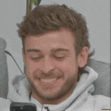 a man with a beard is smiling with his eyes closed while holding a cell phone