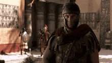 a roman soldier with a helmet on stands in front of a wall with images of people on it