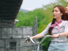 a woman wearing a striped shirt and a pink scarf rides a bike