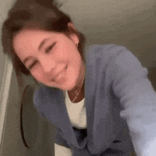 a woman in a blue cardigan is smiling and taking a selfie in a bathroom .