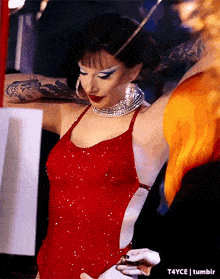 a woman in a red dress is standing next to a woman with red hair and a tattoo on her arm