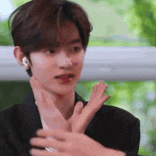 a young man in a black jacket is making a funny face with his hands .