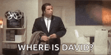 a man in a suit is standing in a living room holding a jacket and saying `` where is david ? ''