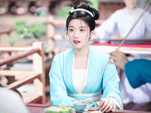 a woman in a blue dress sits at a table with chopsticks