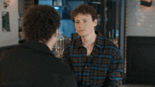 a man in a plaid shirt is talking to another man in a black jacket