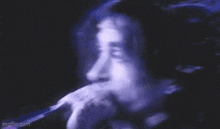 a man is singing into a microphone in a dark room with purple lights behind him .