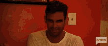 a man sitting in front of a red wall with a bravo logo on the bottom right