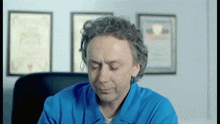 a man in a blue shirt is sitting in front of framed pictures