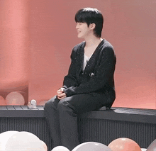 a man in a black sweater is sitting on a ledge with balloons in the background .