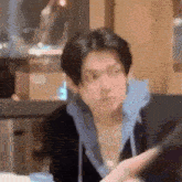 a young man in a blue hoodie is sitting at a table looking at his phone .