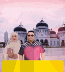 a man and a woman are posing in front of a mosque