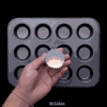 a person is holding a cupcake liner in front of a muffin pan that says mr.cakes on the bottom