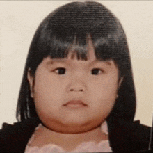 a little girl with a very thick neck is wearing a pink dress and a black jacket .