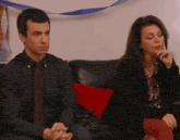 a man in a plaid shirt and tie sits next to a woman who is sitting on a couch