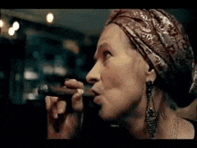 a woman is smoking a cigar and wearing a head scarf .