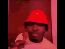 a man wearing a red bucket hat is pointing at the camera .