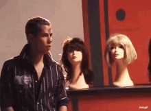 a man in a striped shirt is standing in front of mannequins with wigs on them