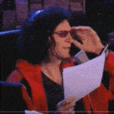 a woman wearing sunglasses holds a piece of paper in front of her face
