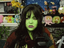 a woman with green paint on her face is sitting in front of a shelf full of stuffed animals .
