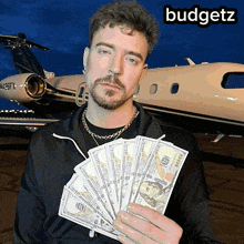 a man holding a bunch of money in front of a plane with the word budgetz on the bottom