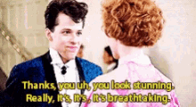 a man in a tuxedo and a woman in a pink dress are talking to each other .