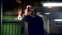 a man is pointing a gun at the camera in front of a red exit sign