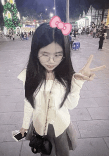 a girl wearing glasses and a hello kitty bow on her hair giving a peace sign