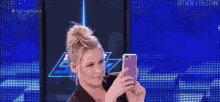a woman is taking a selfie with her cell phone in front of a blue screen .