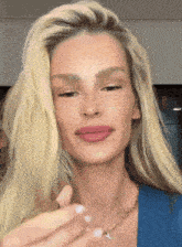 a woman with blonde hair is wearing a blue shirt and a necklace with a letter a on it