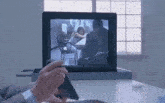 a man is sitting at a desk holding a cell phone in front of a computer monitor .