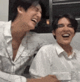 two young men are laughing together while sitting next to each other in a room .