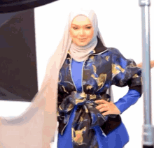 a woman wearing a hijab and a blue jacket stands in front of a white background